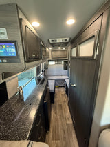 RV rental interior showcasing a modern kitchen with a sink & stovetop, digital display panel, and comfortable rear seating area.