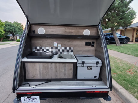 Open rear galley of an RV rental camper with outdoor kitchen: sink, stovetop, and K2 cooler, ready for camping trips.