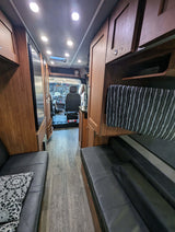 RV rental interior: A cozy camper van with wood cabinets, black seating, and modern lighting, looking towards the cockpit.