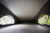 Cozy RV rental pop-top interior. View from the sleeping platform, with canvas walls and windows revealing lush trees.