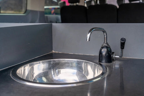Compact stainless steel sink and chrome hand-pump faucet in an RV rental, for essential onboard kitchen needs.
