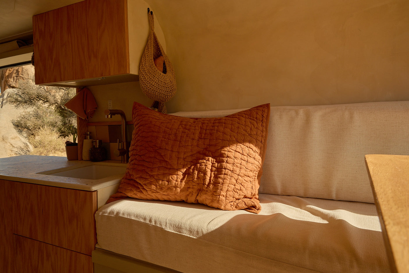 Cozy RV rental interior with a compact kitchen, comfy bench, and a terracotta pillow bathed in desert sunlight.