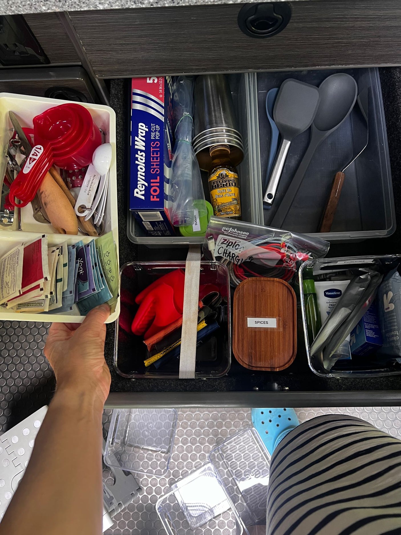 Inside an RV rental, a well-organized drawer holds kitchen utensils, spices, toiletries, charging cables, and foil for travel.