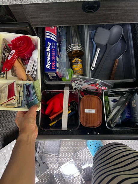 Inside an RV rental, a well-organized drawer holds kitchen utensils, spices, toiletries, charging cables, and foil for travel.