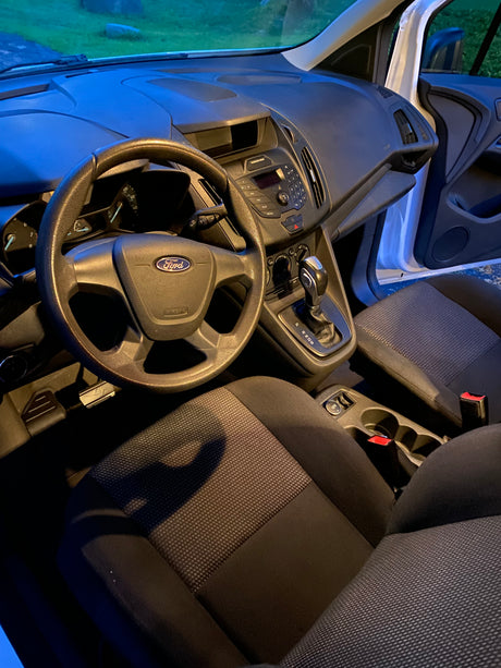 Inside a Ford van: dashboard, steering wheel, gear shift, and fabric seats. Ideal for your next compact rv rental adventure.