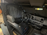 Inside this RV rental: driver's cabin with Mercedes dashboard & insulated privacy shades. A longboard hints at adventure.