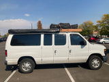 White camper van with roof rack and awning, parked on asphalt. An ideal RV rental for travel and adventures.