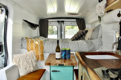 Bright RV rental interior: cozy bed, teal fridge, wooden countertop with sink, and cooktop in a custom camper van.