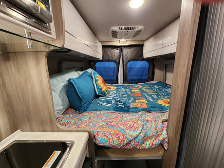 Step inside this RV rental: a snug camper van with a vibrant bed, overhead storage, and compact kitchen area for travel.