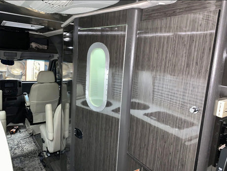 Interior of an RV rental, showcasing the driver's cabin with swivel chairs, and a modern wooden door with an oval porthole.