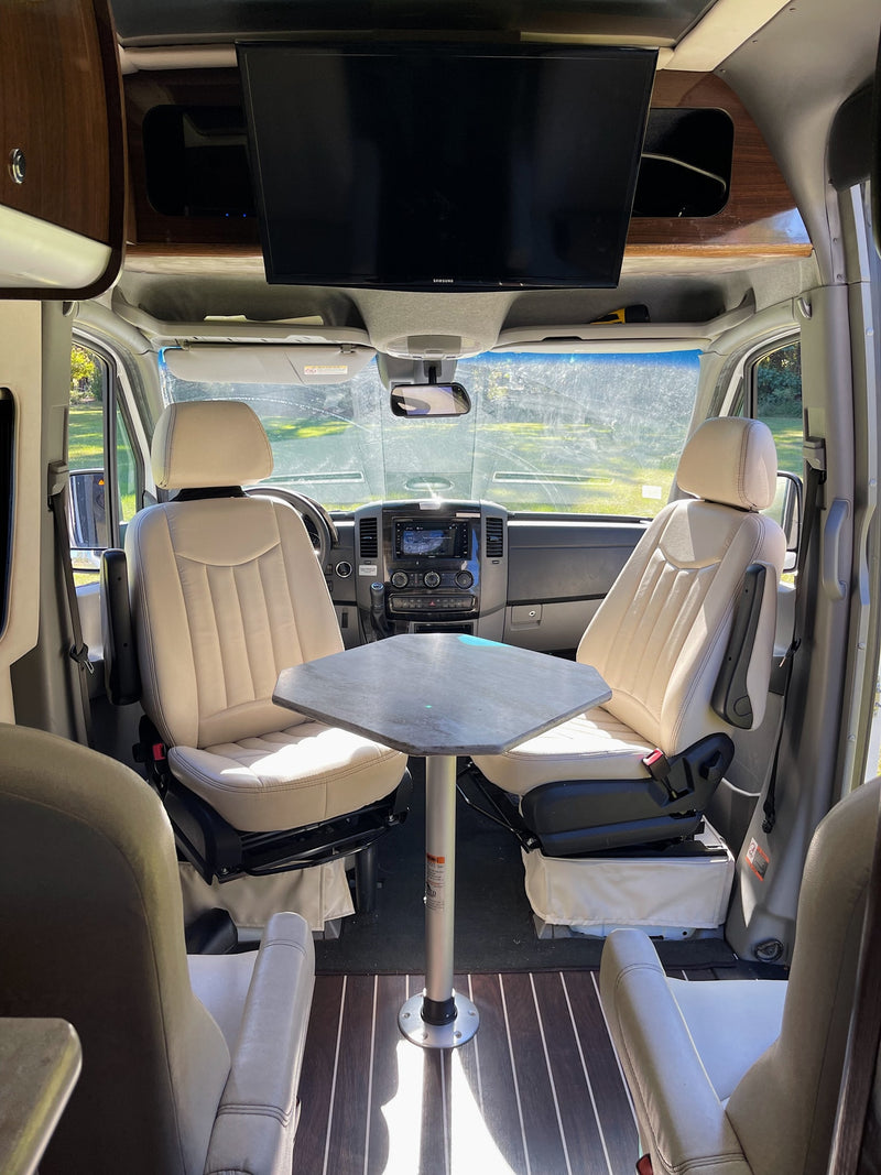 Spacious RV rental interior featuring swiveling front seats, a dining table, and an overhead TV for comfortable living. — photo 6