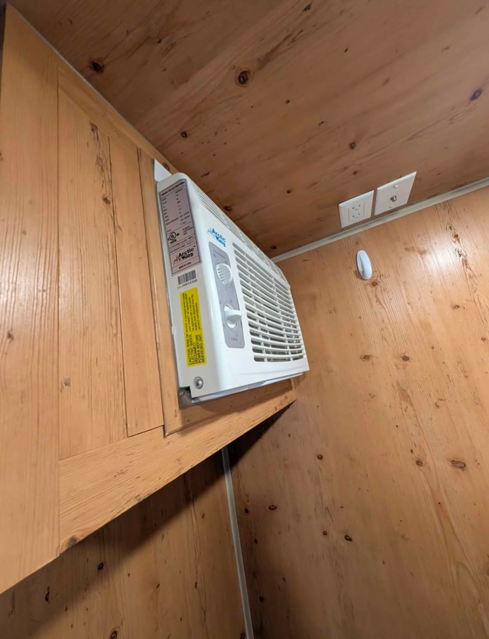 RV rental: Angled view of a wall-mounted AC unit within wood paneling. Includes power & cable outlets, plus a Command hook.
