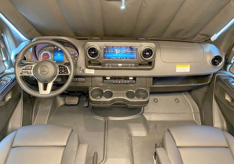 Front interior of an RV rental: Mercedes dashboard with large display, steering wheel, and convenient cupholders.