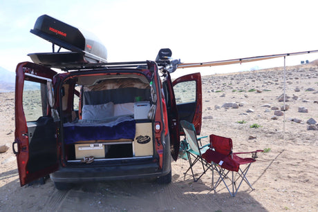 Compact RV rental: a camper van with open back doors revealing bed & storage. Features Yakima box & awning for camping.