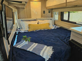 Comfortable RV rental interior featuring a large bed with cozy bedding, TV, and window. Ideal for mobile living.
