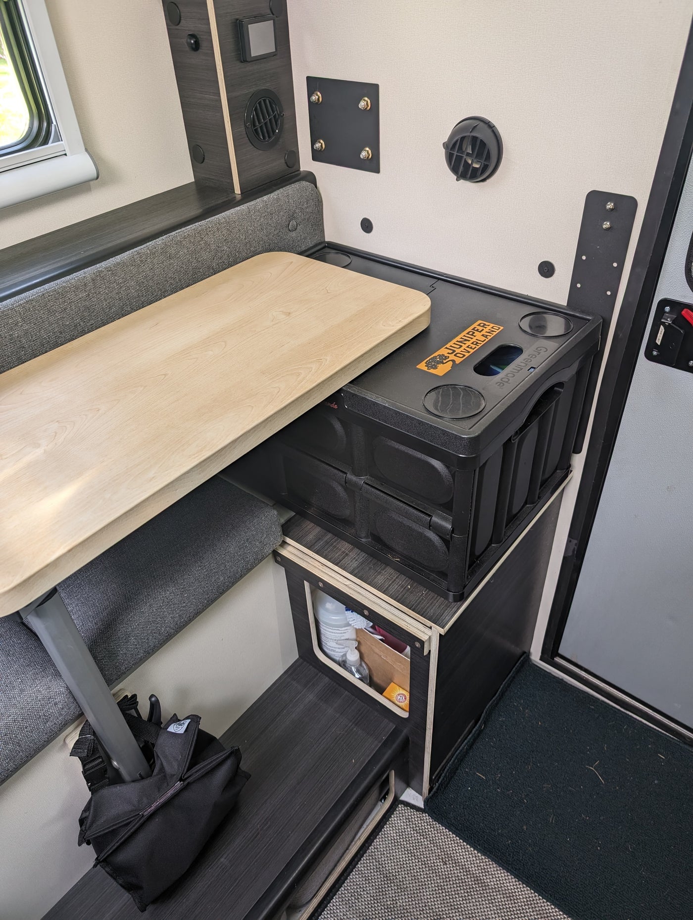 This RV rental's dinette area features a light wood table, compact storage bins, and various onboard controls. — photo 13