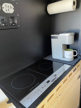 An RV rental's compact kitchen with Cuisinart induction cooktop, Keurig coffee maker, and controls, perfect for travel.