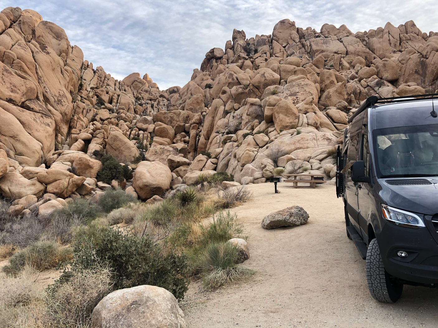 Discover vast desert landscapes with an rv rental. Parked black campervan at a scenic campsite among massive rock formations.