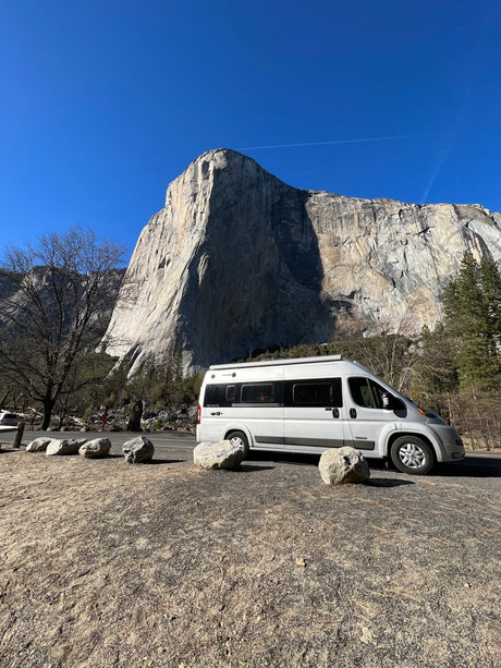 An rv rental camper van rests before Yosemite's El Capitan, a towering granite cliff under a clear sky. A perfect scenic travel spot!