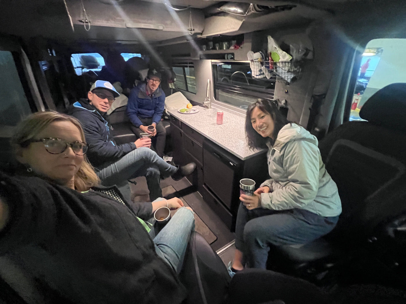 Four people relax in their RV rental, showcasing the compact and functional interior with a kitchen counter and overhead storage.
