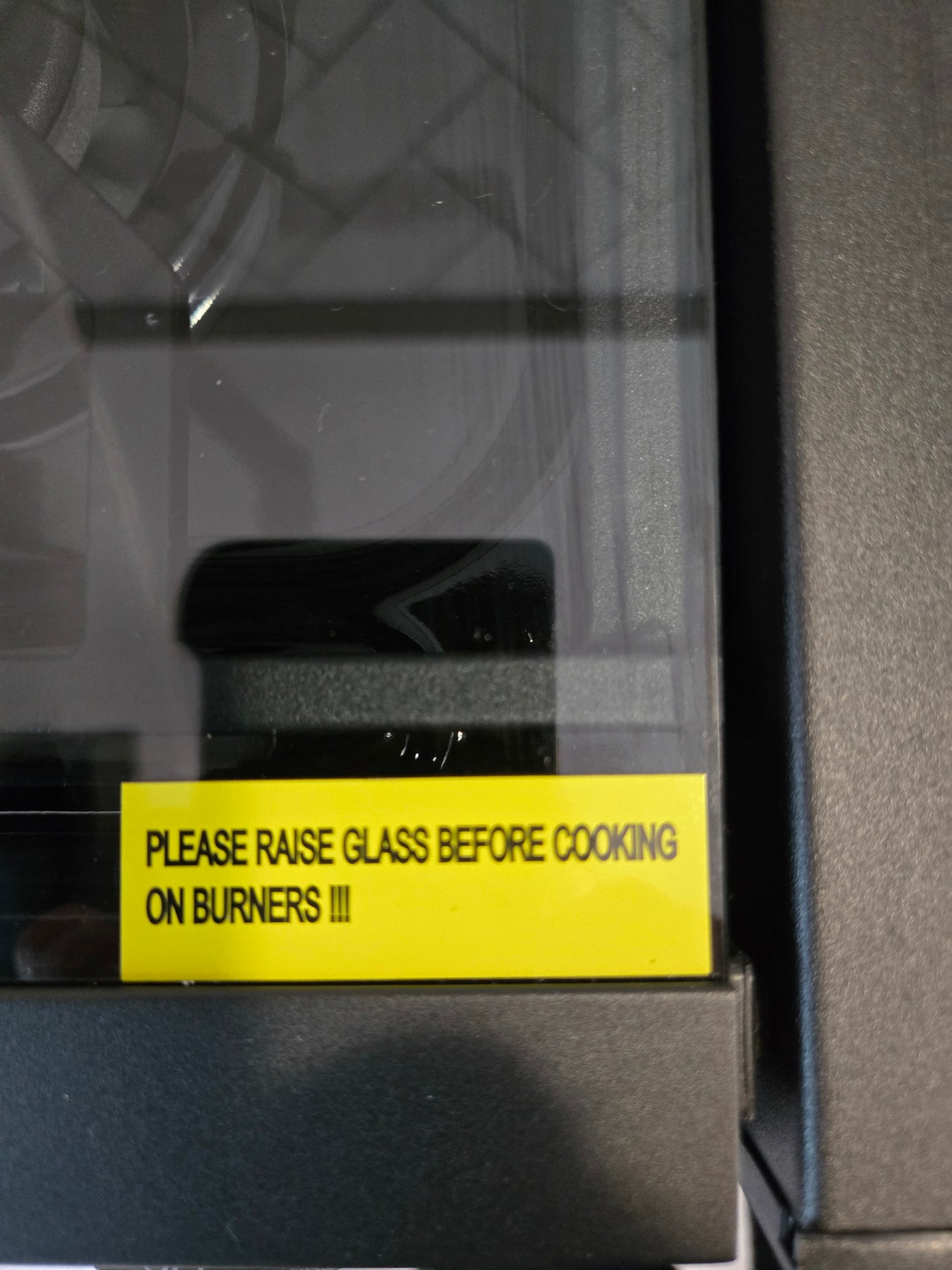 RV rental stove with a warning to raise glass cover before cooking on burners.