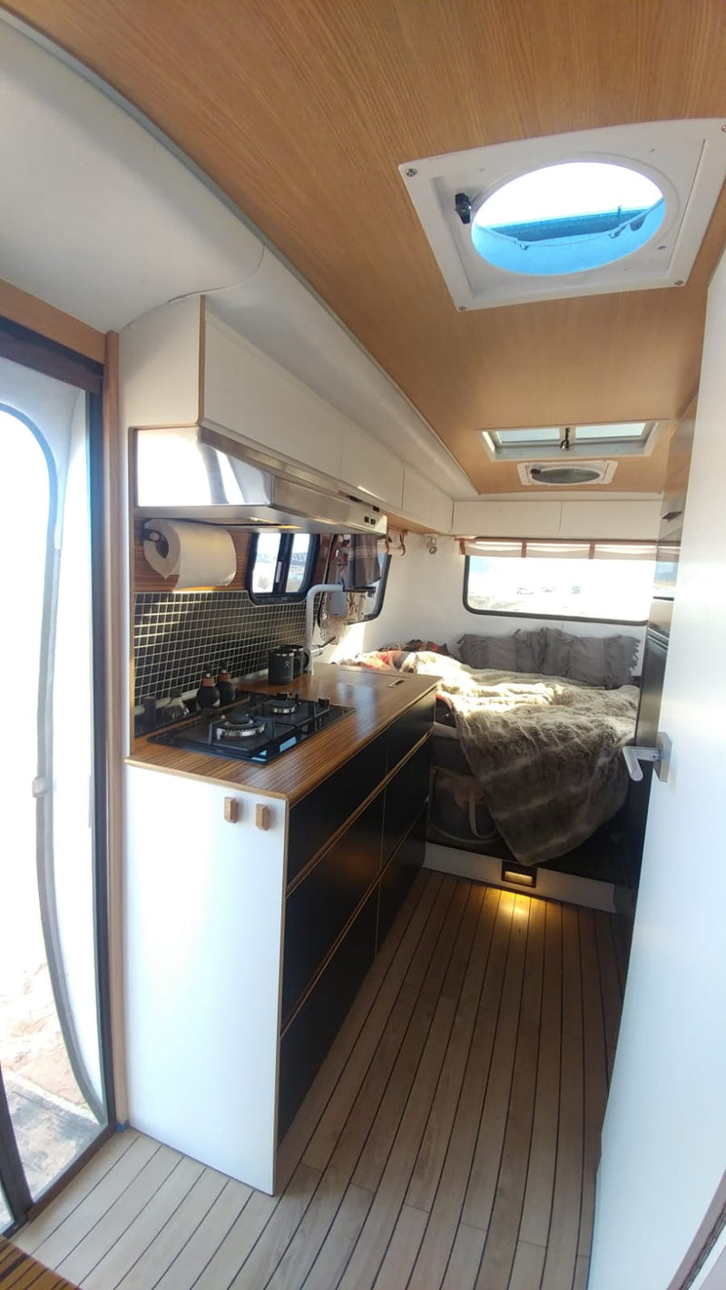Discover this modern RV rental interior, featuring a well-equipped kitchen with stove, a comfortable bed, and sleek wood accents. — photo 6