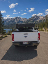 RV rental pickup truck with a roof-top tent overlooks a scenic mountain lake and snowy peaks. Ideal for outdoor adventures.