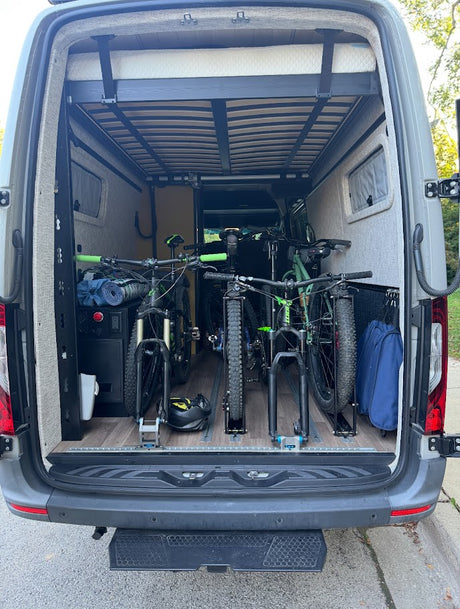 Rear of RV rental: elevated bed over secure racks holding multiple mountain bikes, ideal for outdoor trips and adventure travel.