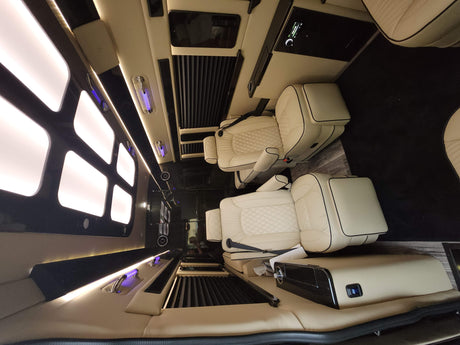 Inside this premium RV rental: A lavish custom van interior with cream quilted seats, sleek black accents & soft lighting.