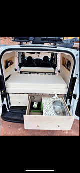 Compact RV rental: White camper van interior with a cozy bed, pull-out kitchen (stove & sink), and built-in storage.