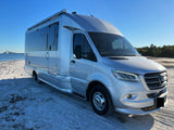 Silver Airstream Atlas luxury rv rental on a sunny beach, a motorhome perfect for scenic adventures with a bridge view.