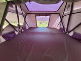 Interior of a cozy rooftop tent setup, featuring a dark mattress, mesh windows, and structural poles, perfect for RV rental adventures.