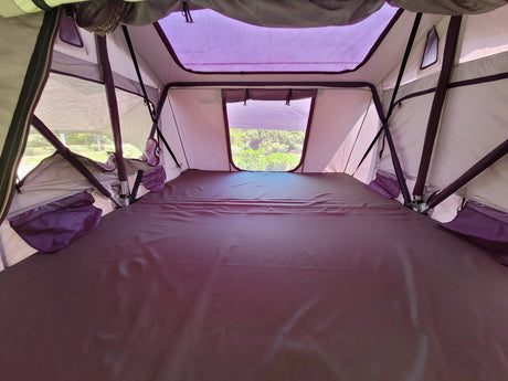 Interior of a cozy rooftop tent setup, featuring a dark mattress, mesh windows, and structural poles, perfect for RV rental adventures.