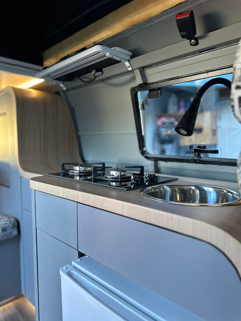 Modern rv rental kitchen featuring a two-burner stove, sink, and light grey cabinets with wood counters. — photo 4