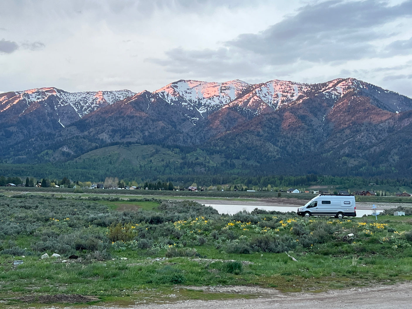 Experience serene nature with an **rv rental**! Snow-capped mountains glow at sunset, overlooking a field and van.