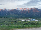 Experience serene nature with an **rv rental**! Snow-capped mountains glow at sunset, overlooking a field and van.