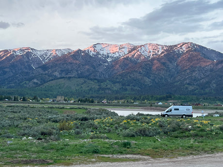 Experience serene nature with an **rv rental**! Snow-capped mountains glow at sunset, overlooking a field and van.