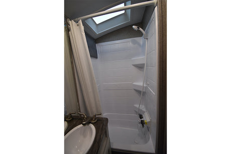 Compact RV rental bathroom with a white shower/tub combo, flexible shower head, skylight, and sink. Functional for travel.
