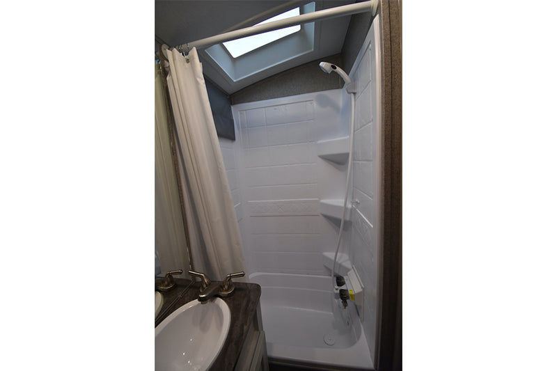 Compact RV rental bathroom with a white shower/tub combo, flexible shower head, skylight, and sink. Functional for travel. — photo 19