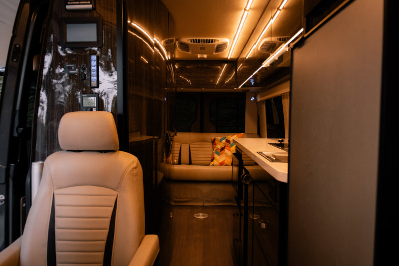 Luxurious RV rental interior with tan seating, modern kitchen, ambient lighting, and control panel for comfortable travel. — photo 12