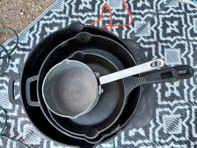 Prepare meals in your RV rental! Stacked cast iron pans & a small pot on an outdoor mat, ready for camping. — photo 16