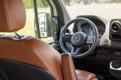 Driver's view in a modern Mercedes RV rental van, showing the steering wheel, dashboard, and custom switch panel.