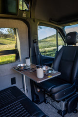 This rv rental features a cozy dining area with a table set for two, swivel passenger seat, and power outlets for comfort.