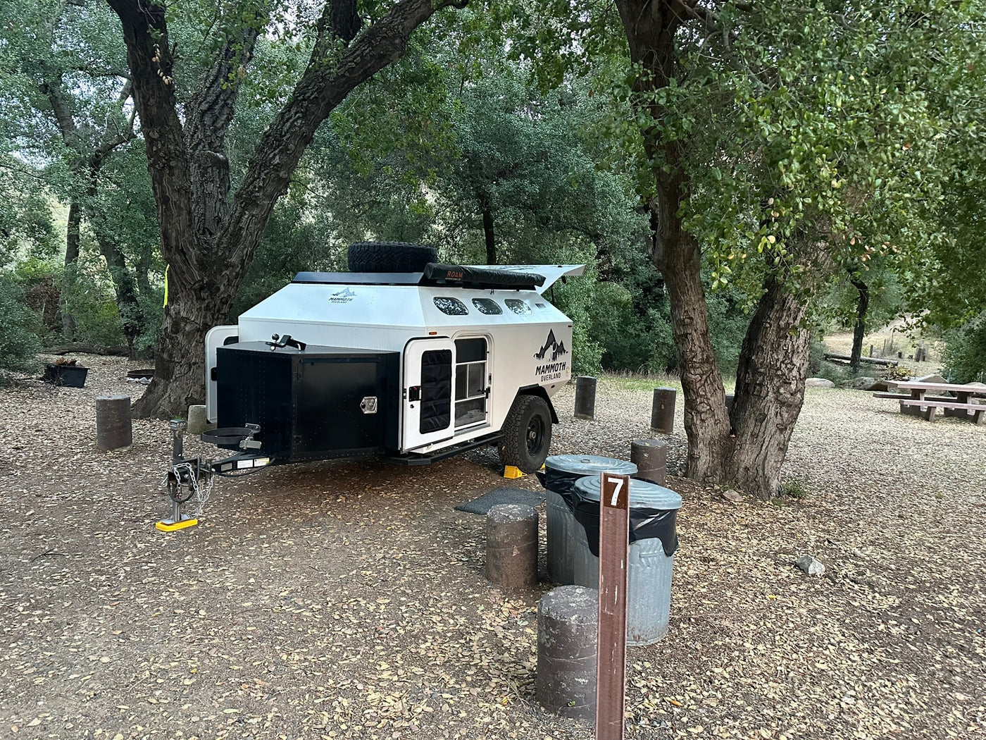  parked among dark rocks for an epic night adventure.|A white overlanding RV rental trailer is parked in a shaded campsite — photo 2