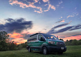 Vibrant sunset over a custom green RV rental van in a grassy field, ready for your next camper adventure.