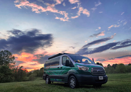 Vibrant sunset over a custom green RV rental van in a grassy field, ready for your next camper adventure.