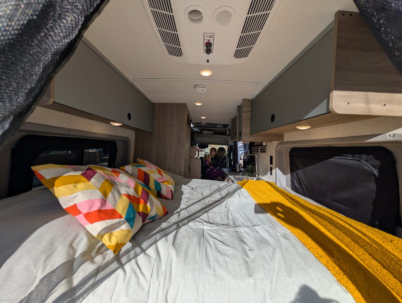Cozy RV rental interior with a comfy bed, kitchen area, and overhead storage, perfect for your next camper van adventure.