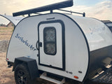 This Bushwhacker 10 HD teardrop RV rental, a compact white camper with off-road tires and roof awning, is ready for adventure.