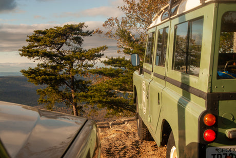 A classic green Land Rover and another 4x4 parked on a rocky mountain overlook. An ideal adventure with an RV rental.