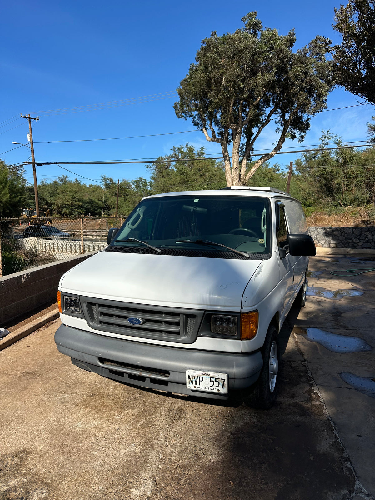 White Ford van, ready for your RV rental journey, parked on a sunny day. Features: LED headlights, Hawaii plate NVP 557.